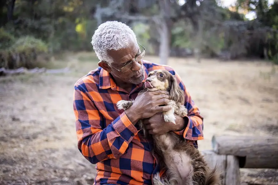 A senior man with a long haired dachshund cuddling outdoors